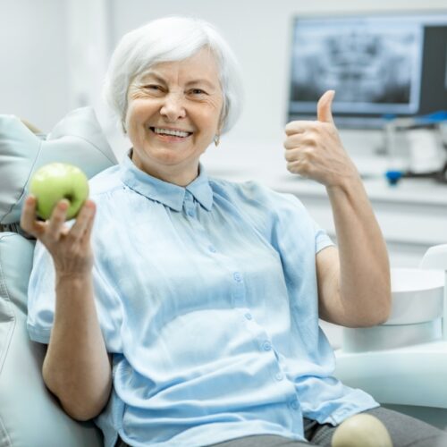 woman at the dentist office holding an apple smiling with thumbs up